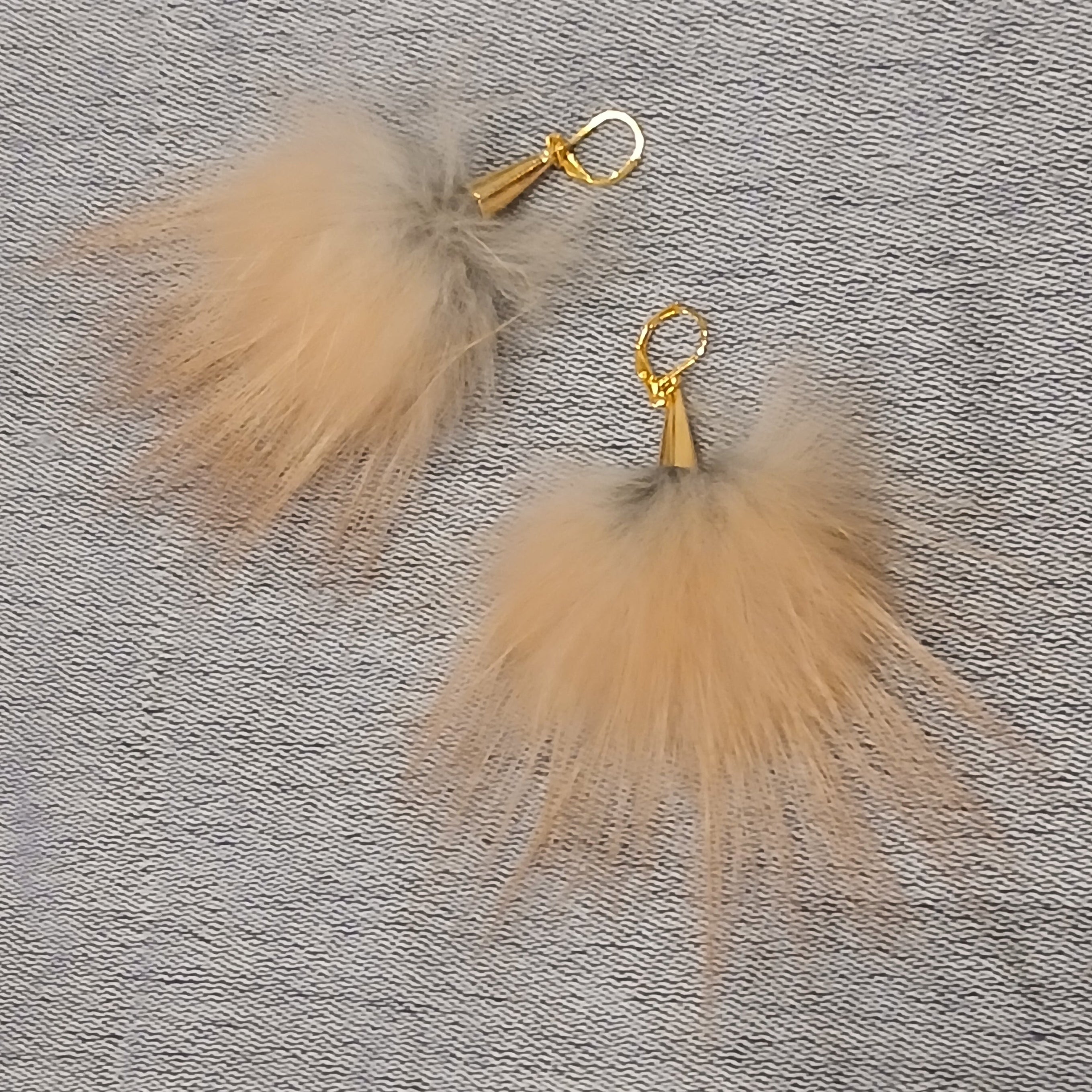 Pair of beige fluffy earrings with gold hooks on a gray textured background
